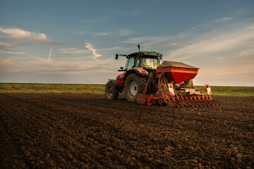 Farmer with tractor seeding in sunset