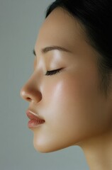 Fototapeta premium an Asian woman with her eyes closed, featuring clear and flawless skin on the front half of her face. She has delicate features and is wearing light makeup