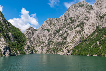 Scenic ferry boat tour on Lake Koman reservoir on Drin river surrounded by forested steep hills, cliffs and majestic rugged mountain ranges of Albanian Alps. Panoramic view along Albanian Fjords. Awe