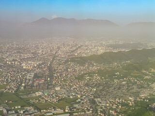 Aerial view from airplane of Tirana city nestled in valley surrounded by Dajti mountains in Albania, Europe.  Layer of pollution creates mist shrouded around ridges. Hazy air quality. Cityscape