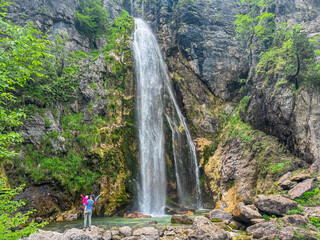 Mother with small child standing under majestic Grunas waterfall cascading down a rocky cliff in...