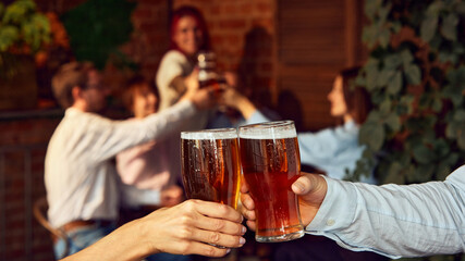 Heart of celebration. Glasses filled with frothy beer clink as sports fans in background react to...