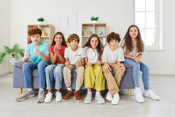 Portrait of a group of children, kids sits on a sofa at home, watching a sports match on television together. Schoolchildren excitement and camaraderie as they enjoy the TV game as friends.