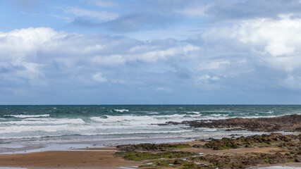 Strandhill beach in Ireland features a rugged rocky shore with waves and wet sand, under a bright blue sky with scattered clouds