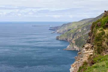 Fototapeta premium The Slieve League cliffs in Ireland rise dramatically from the Atlantic, with rugged rocks leading down to the sea. The composition draws the eye along the jagged coastline