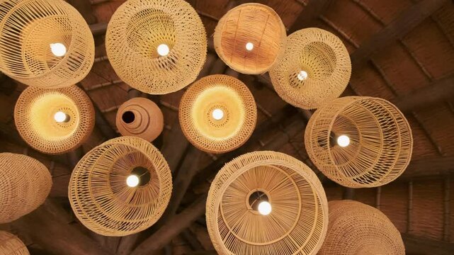 Many woven African lamps shades suspended from a thatch roof ceiling
