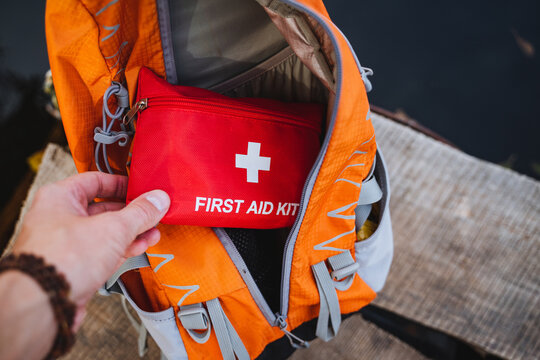 A person is standing with a first aid kit prominently displayed in front of a bright orange backpack, showcasing essential emergency items that are crucial for safety and preparedness