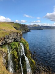 Two waterfalls cascading directly into the sea at the Arnarstapi coast in Iceland surrounded by basalt rock cliffs