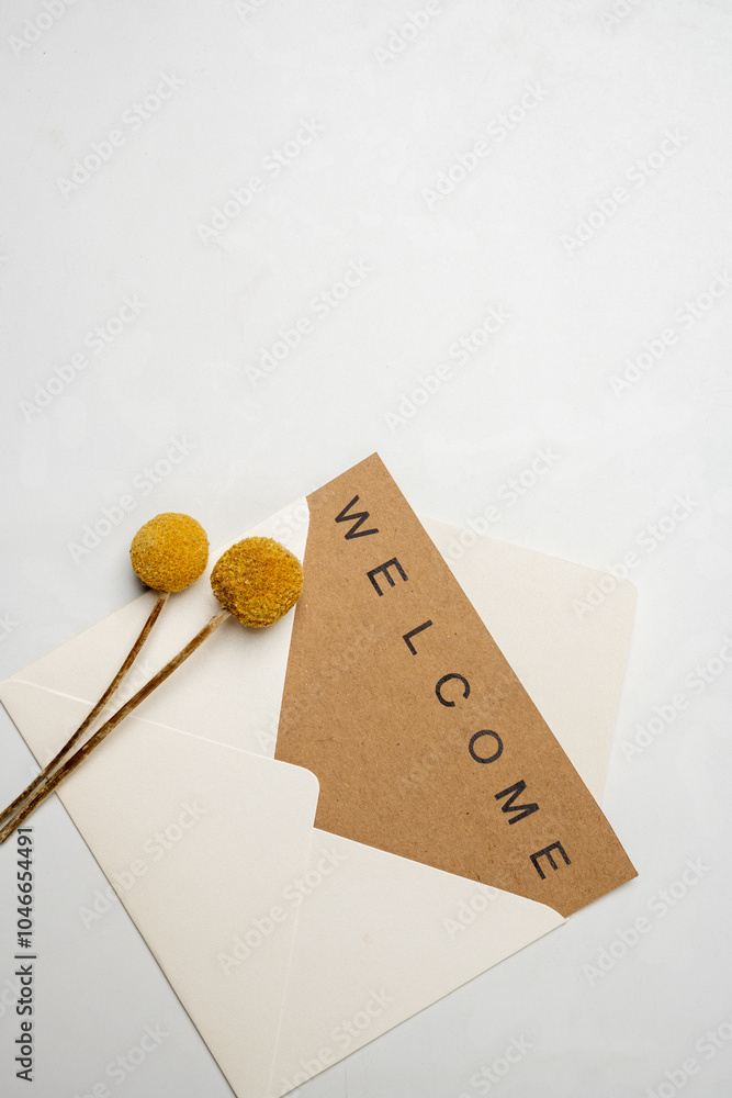 Poster top view of white envelope and postcard with brown card with words welcome and flowers on it. welcom