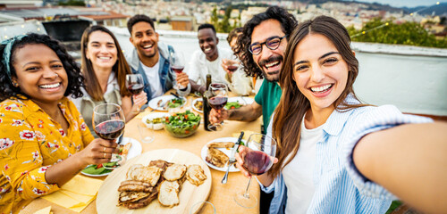 Happy friends having fun at rooftop dinner party - Group of young people taking selfie photo at outdoors dining table - Life style concept with guys and girls eating food and drinking wine together