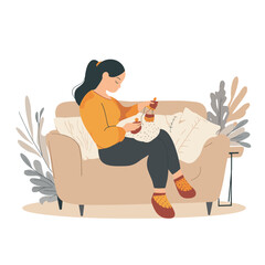 A pregnant woman knitting baby booties on a couch