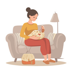 A pregnant woman knitting baby booties on a couch