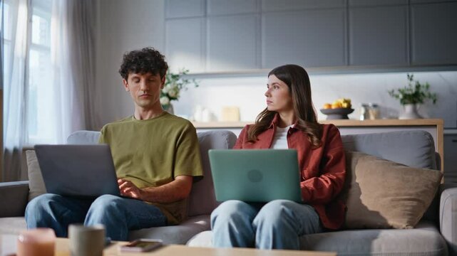 Home sweethearts browsing laptops at soft couch place. Young couple working