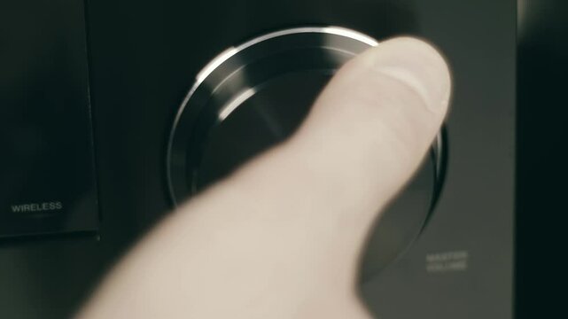 A man's hand turns a round, black, shiny volume knob on an amplifier. Closeup. Macro. Shallow depth of field
