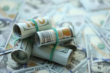 Many rolls of one hundred dollar bills lies on big amount of american currency banknotes