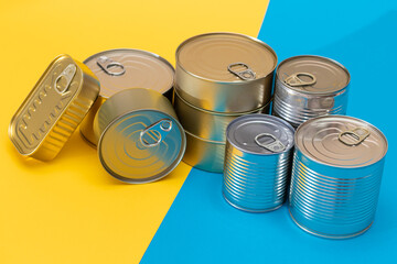 A Group of Stacked Tin Cans on Split Blue and Yellow Background. Canned Food. Aluminum Cans for Safe and Long Term Storage of Food. Steel Sealed Food Storage Containers