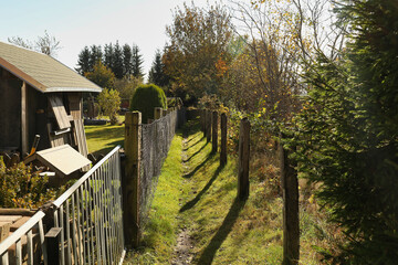 Fototapeta premium Schmaler Wanderweg entlang von Gartenzäunen in Neuhaus-Igelshieb, herbstlicher Pfad am Rennsteig, Thüringer Wald, Landkreis Sonneberg, Thüringen, Deutschland, Wandern im Schiefergebirge im Herbst