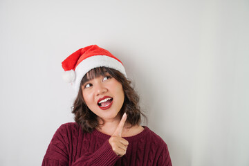 Excited young asian woman wearing santa clause hat and red long sleeved sweater with smiling face expression, isolated over white background. Concept for Christmas Holiday and New Year Party