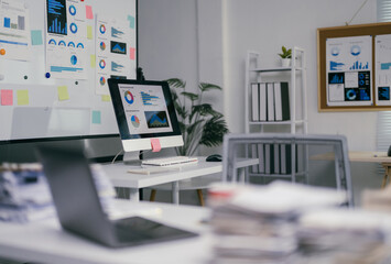 Modern office with nobody present showing financial charts and data on computer screen and on a whiteboard, concept of workplace