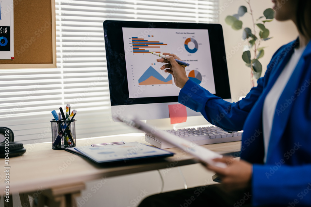 Poster businesswoman is sitting at her desk and analyzing financial data on her computer. she is pointing a