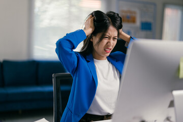 Young businesswoman is experiencing stress and frustration while working on her computer, visibly...