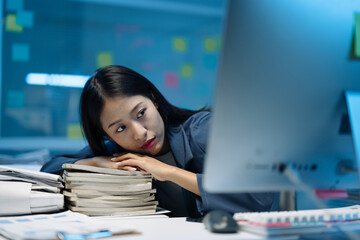 Exhausted businesswoman resting her head on a large stack of folders, feeling overwhelmed by the...