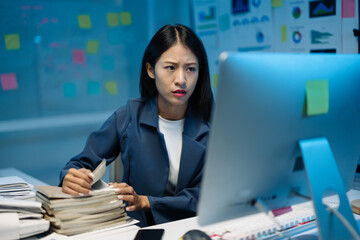 Asian businesswoman is feeling stressed while working late at night in the office, searching for...