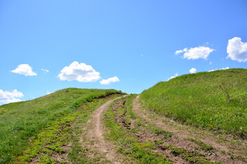 a dirt road with green grass going up the blue sky with clouds copy space