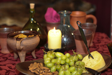 A classic still life composition, elegantly set table reminiscent of traditional castle banquet scenes. The warm glow of a single burning candle illuminates the rustic arrangement of grape