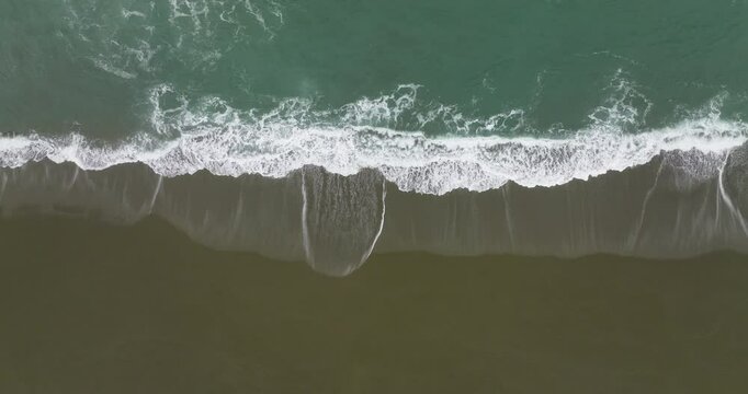 Bird's eye tracking aerial above waves breaking on Cape Blanco State Park beach, Oregon coast.
