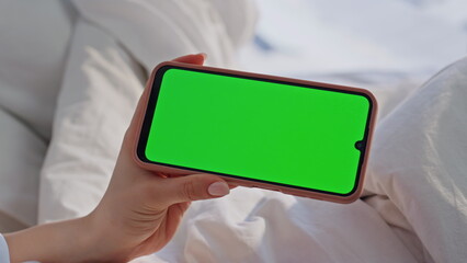 Woman watching chromakey smartphone in comfortable bed at home morning closeup.