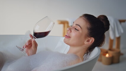 Smiling lady enjoying wine in bubble bath luxury home closeup. Woman drinking