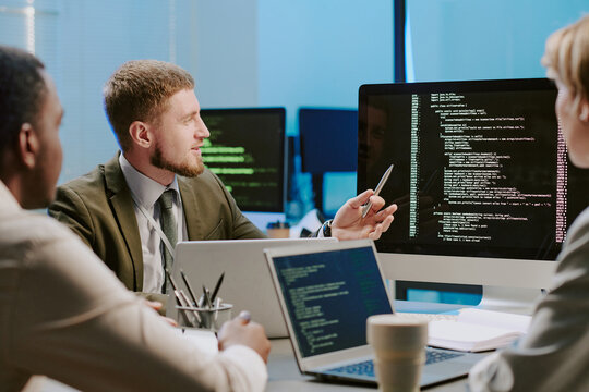 Group of three diverse young cybersecurity specialists discussing issues during meeting in office equipped with modern computers