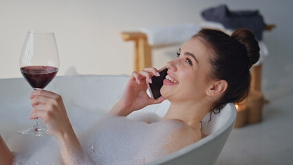 Calling girl relaxing bathtub holding wine glass closeup. Woman lying spa bath