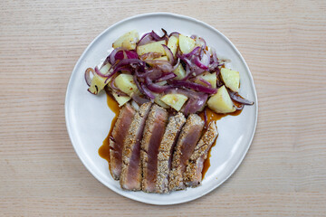 A plate of tuna steak with roast potato and onion.