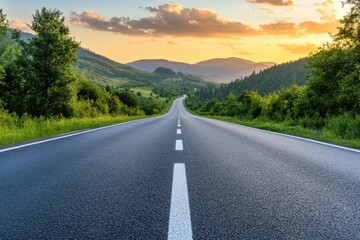 A winding asphalt road leads through a mountainous valley towards a stunning sunset.