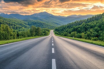 A winding asphalt road leads through lush green forests and mountains towards a stunning sunset sky.