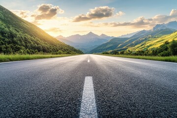 A straight asphalt road leading into the distance between mountains and hills with a bright sky, clouds and a setting sun.