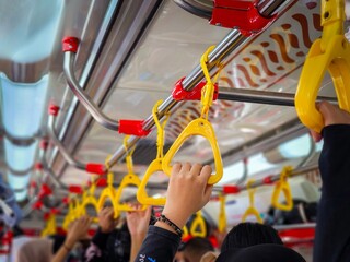 In the crowded train, a person was standing and holding a yellow handle hanging at the top of the...