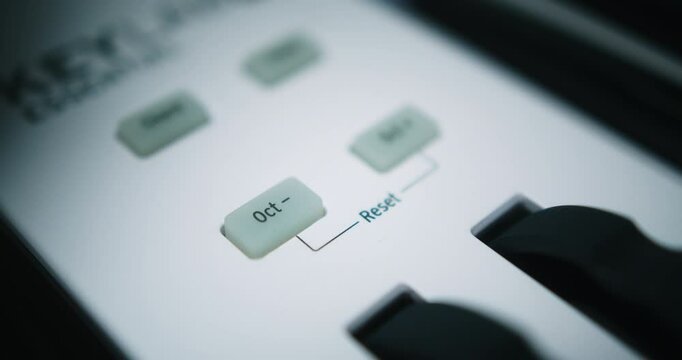 Beautiful slow motion and close-up shot. Musician presses the button to reduce an octave on his Arturia midi keyboard to record a song in his home studio.