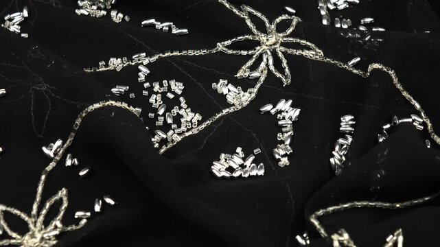 Silver beads are scattered on black chiffon with bead embroidery. Handicrafts and sewing, background