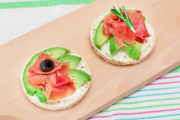 Rice Cake Sandwich with Avocado, Jamon, Olives and Rosemary on Wooden Cutting Board. Easy Breakfast. Quick and Healthy Sandwiches. Crispbread with Tasty Filling. Healthy Dietary Snack