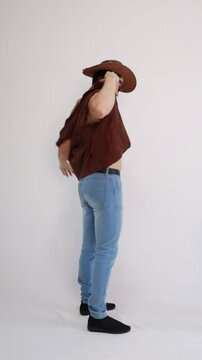 Modelo masculino vaqueiro da moda usando jeans e colete marrom e chap&eacute;u 