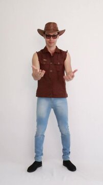 Modelo masculino vaqueiro da moda usando jeans e colete marrom e chap&eacute;u 