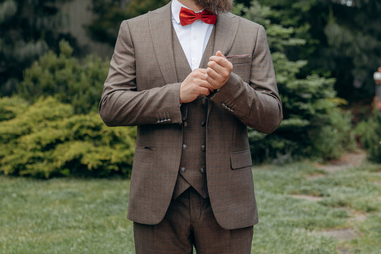 A man with  in a stylish suit  fixes a bow tie. Morning of the groom. Bride helps to fix the groom jacket and accessories