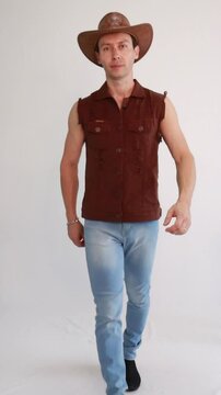 Modelo masculino vaqueiro da moda usando jeans e colete marrom e chap&eacute;u 
