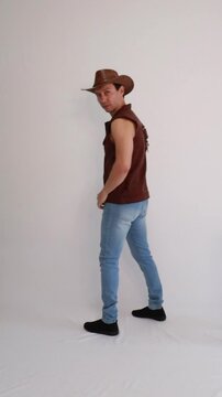 Modelo masculino vaqueiro da moda usando jeans e colete marrom e chap&eacute;u 
