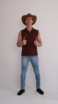 Modelo masculino vaqueiro da moda usando jeans e colete marrom e chap&eacute;u 