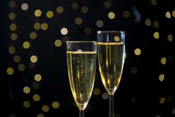 Champagne bubbling in two glasses while blurred golden confetti falling in the background with...
