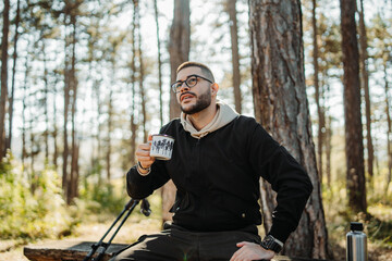 Young caucasian man drinking water taking break from hiking or trekking